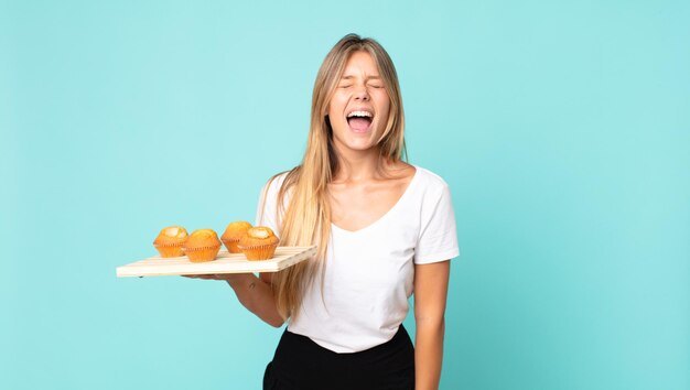 Junge blonde frau, die aggressiv schreit, sehr wütend aussieht und einen muffins-troy hält