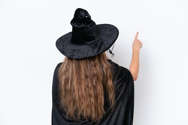 Junge blonde Frau, die als Hexe verkleidet ist, isoliert auf weißem Hintergrund, die mit dem Zeigefinger nach hinten zeigt