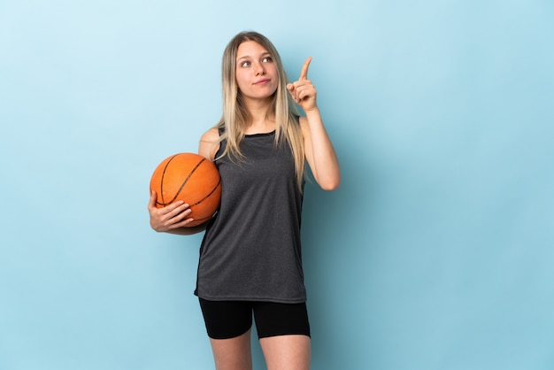 Junge blonde Frau, die Basketball lokalisiert auf blauer Wand spielt