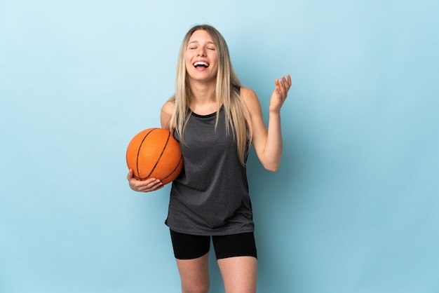 Junge blonde Frau, die Basketball spielt, der auf lachenden blauen Wand lokalisiert wird