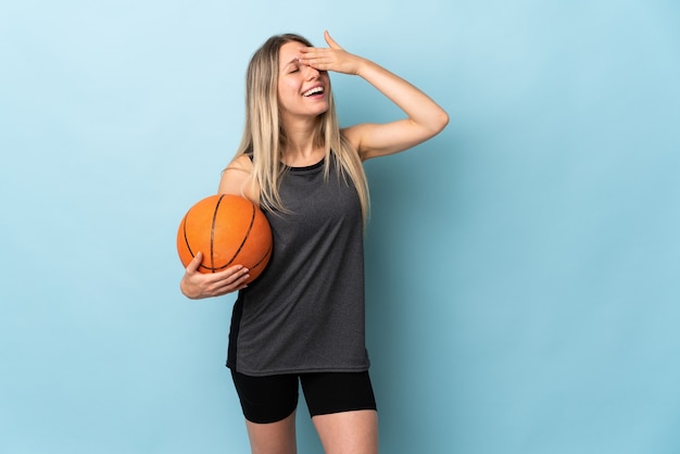 Junge blonde Frau, die Basketball spielt, isoliert auf blauem Lachen