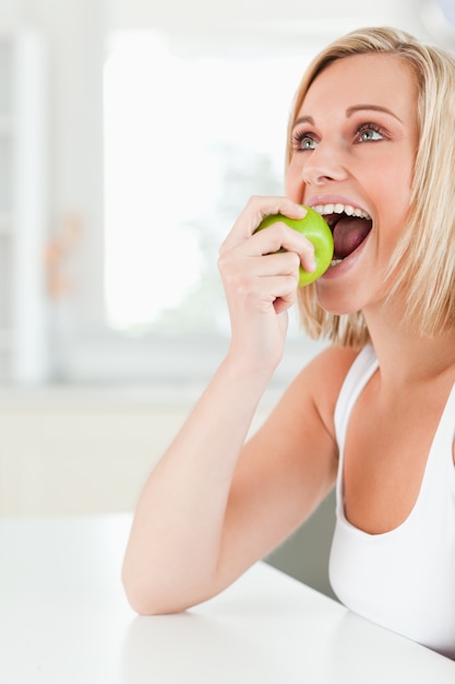 Junge blonde Frau, die bei Tisch sitzt, einen Apfel essend