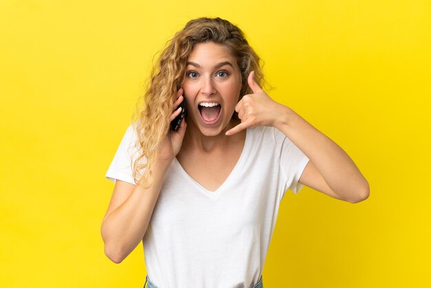 Junge blonde Frau, die das Handy lokalisiert auf gelbem Hintergrund verwendet, das Telefongeste macht. Ruf mich zurück Zeichen