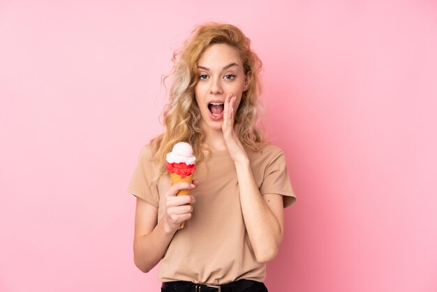 Junge blonde Frau, die ein Kornett-Eis auf rosa schreiend mit Mund weit offen hält