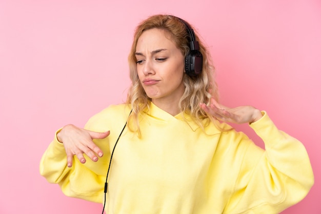 Junge blonde Frau, die ein Sweatshirt trägt, das auf rosa Wand lokalisiert Musik hört und tanzt