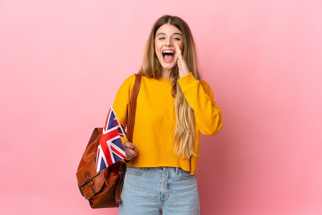 Junge blonde Frau, die eine britische Flagge lokalisiert auf weißem Raum hält, der mit Mund weit offen schreit
