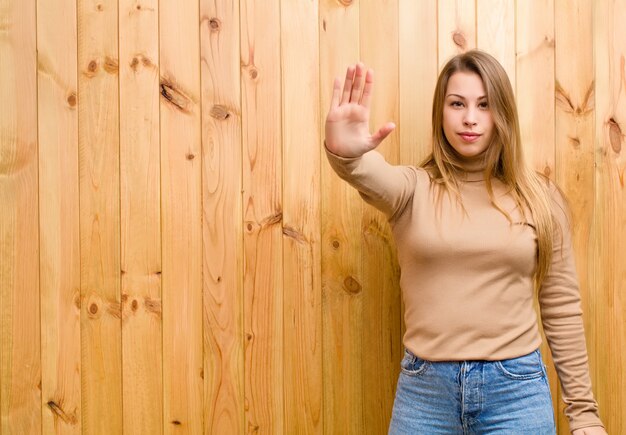 Junge blonde Frau, die ernst, streng, unzufrieden und wütend aussieht und offene Handfläche zeigt, die Stoppgeste macht