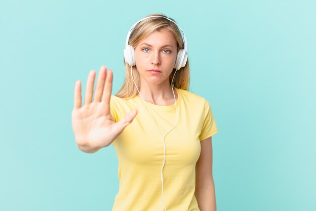 Junge blonde Frau, die ernsthafte offene Handfläche zeigt, die Stoppgeste macht und Musik hört.