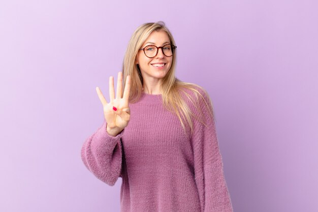 Junge blonde Frau, die freundlich lächelt und aussieht und Nummer vier zeigt