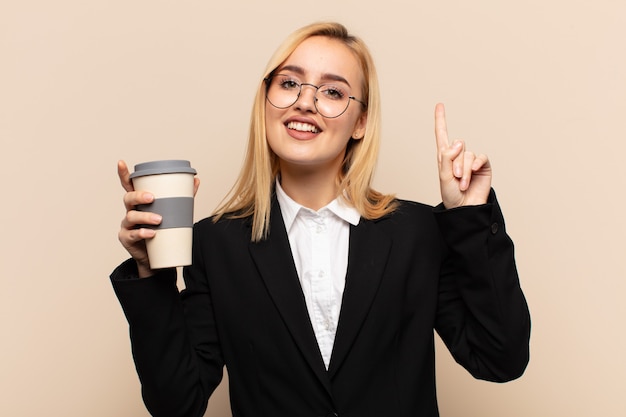 Foto junge blonde frau, die fröhlich und glücklich lächelt und mit einer hand nach oben zeigt