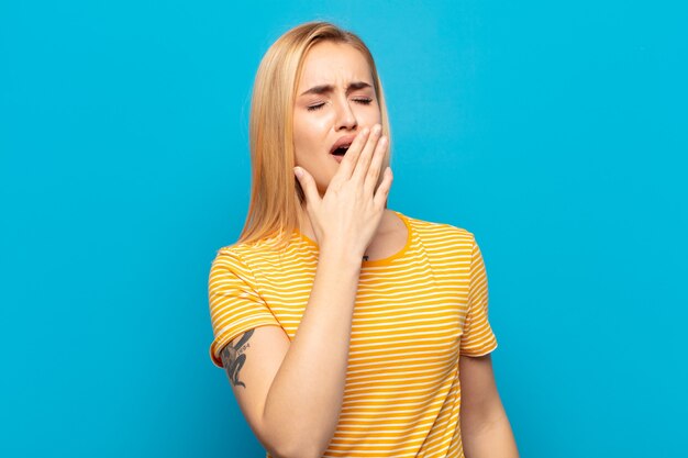 junge blonde Frau, die früh am Morgen faul gähnt, aufwacht und schläfrig, müde und gelangweilt aussieht