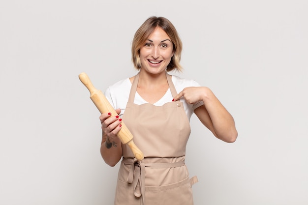 Junge blonde Frau, die glücklich, überrascht und stolz ist und mit einem aufgeregten, erstaunten Blick auf sich selbst zeigt