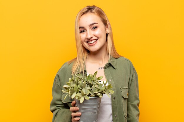 Junge blonde Frau, die glücklich und doof mit einem breiten, lustigen, verrückten Lächeln und weit geöffneten Augen schaut