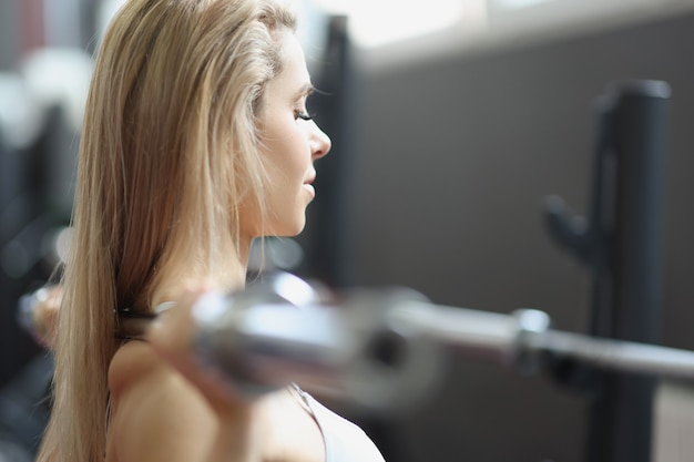 Junge blonde Frau, die Hantel im Fitnessstudio hebt