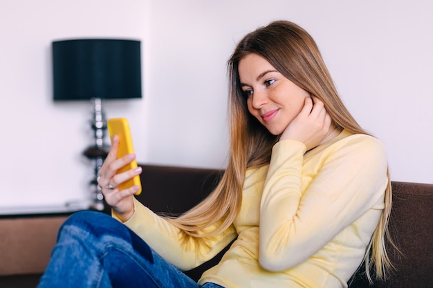 Junge blonde Frau, die ihr Smartphone drinnen benutzt