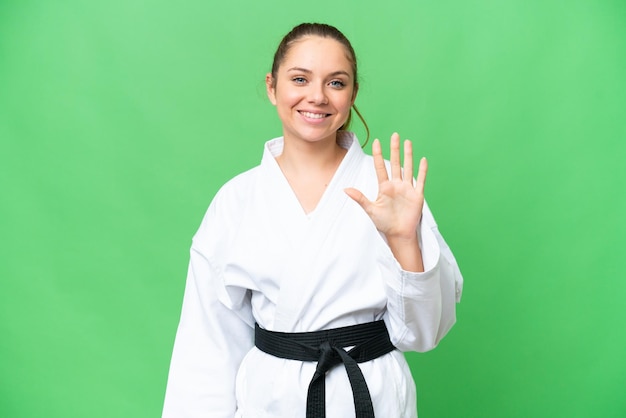Junge blonde Frau, die Karate über isoliertem Chroma-Key-Hintergrund macht und fünf mit den Fingern zählt