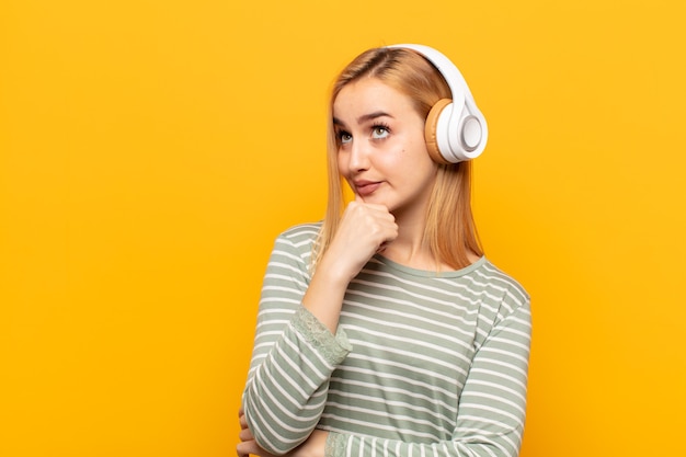 Junge blonde Frau, die nachdenklich fühlt, sich wundert oder Ideen vorstellt, Tagträumen und aufschaut, um Raum zu kopieren