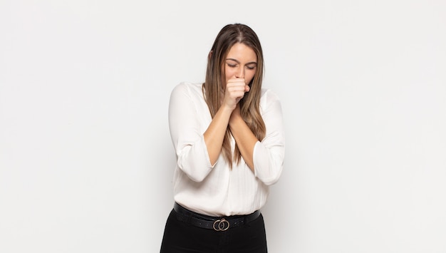 Junge blonde Frau, die sich mit Halsschmerzen und Grippesymptomen krank fühlt und mit bedecktem Mund hustet