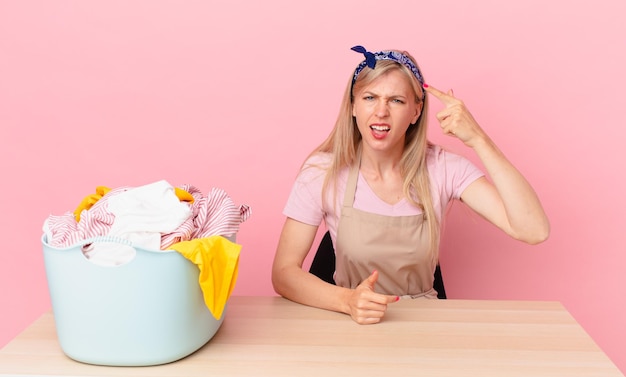 Junge blonde Frau, die sich verwirrt und verwirrt fühlt und zeigt, dass Sie verrückt sind. Wäsche waschen Konzept