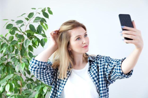 Junge blonde Frau, die Smartphonebildschirm auf Weiß hält