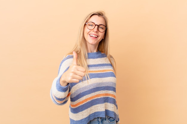 Junge blonde Frau, die stolz ist und positiv mit Daumen nach oben lächelt