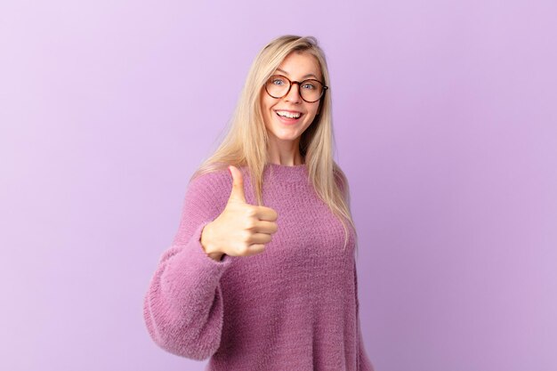 Junge blonde Frau, die stolz ist und positiv mit Daumen nach oben lächelt