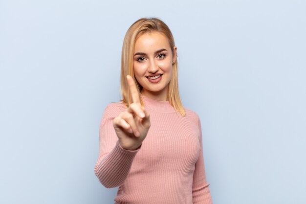 Foto junge blonde frau, die stolz und zuversichtlich lächelt und nummer eins triumphierend posiert und sich wie ein anführer fühlt