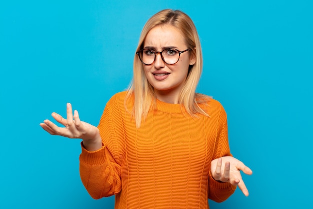 Junge blonde Frau, die verwirrt, verwirrt und gestresst aussieht, sich zwischen verschiedenen Optionen wundert und sich unsicher fühlt