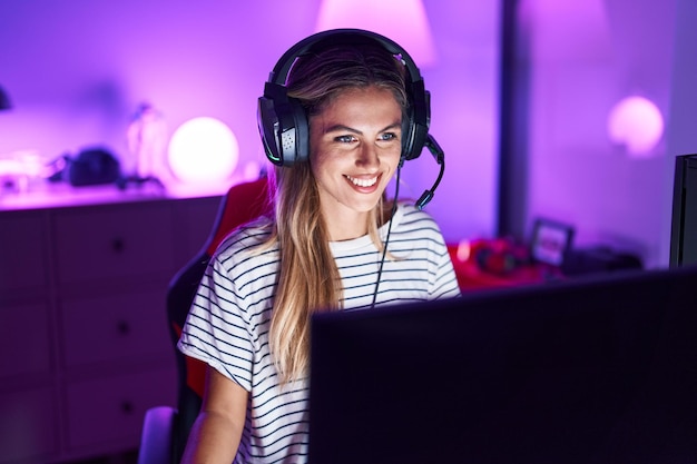 Junge blonde Frau, die Videospiele spielt, sieht positiv und glücklich aus und lächelt mit einem selbstbewussten Lächeln, das Zähne zeigt