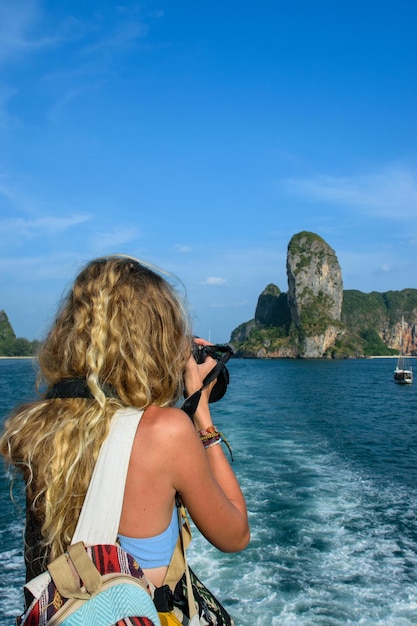 Junge blonde Frau, die vom Deck eines Bootes aus ein Foto auf einer Insel macht
