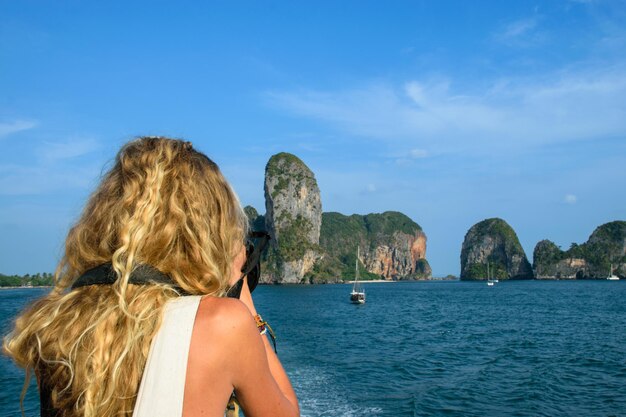 Junge blonde Frau, die vom Deck eines Bootes aus ein Foto auf einer Insel macht