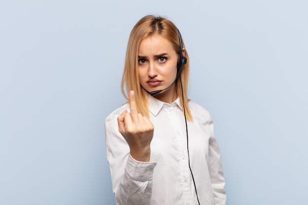 Junge blonde Frau, die wütend, genervt, rebellisch und aggressiv ist, den Mittelfinger dreht und zurückschlägt