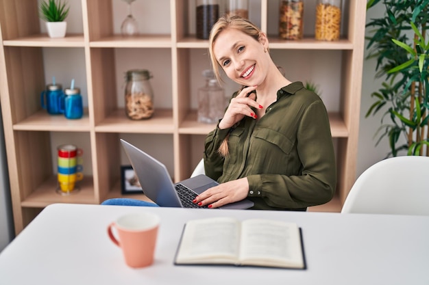 Junge blonde Frau, die zu Hause Kaffee mit Laptop trinkt