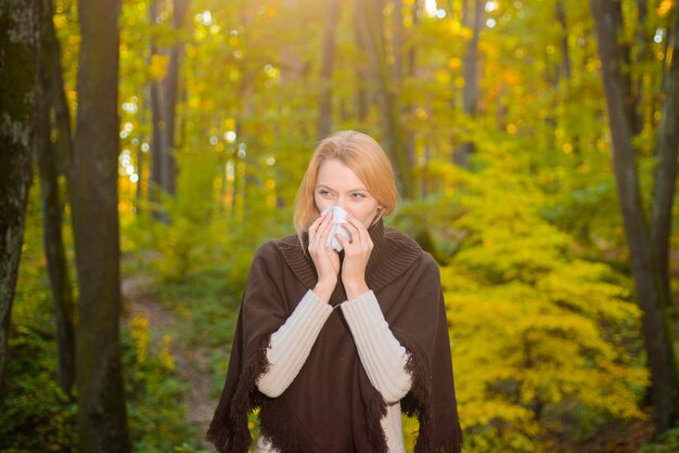 Junge blonde Frau geht im herbstlichen Parkmädchen in warmer Pulloverfrau mit Servietten-Influenza-Krankheit