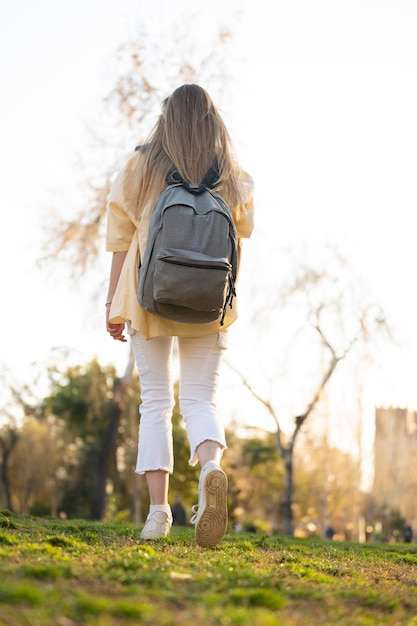 Junge blonde Frau geht und schaut sich mit ihrem Rucksack im Park um