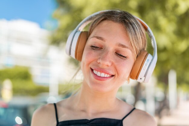 Foto junge blonde frau hört draußen musik