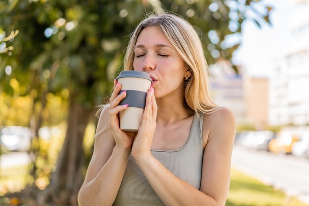 Junge blonde Frau im Freien hält einen Kaffee zum Mitnehmen in der Hand