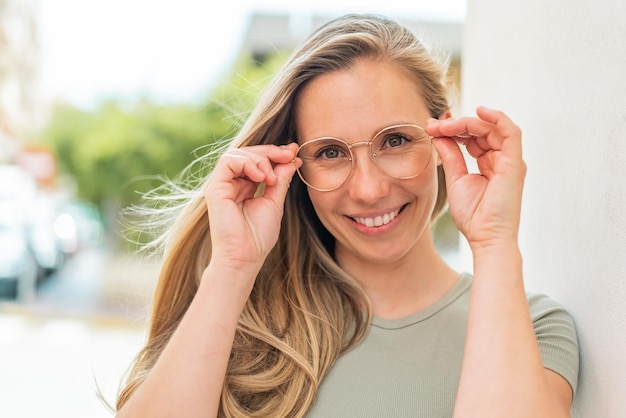 Junge blonde Frau im Freien mit Brille mit fröhlichem Gesichtsausdruck