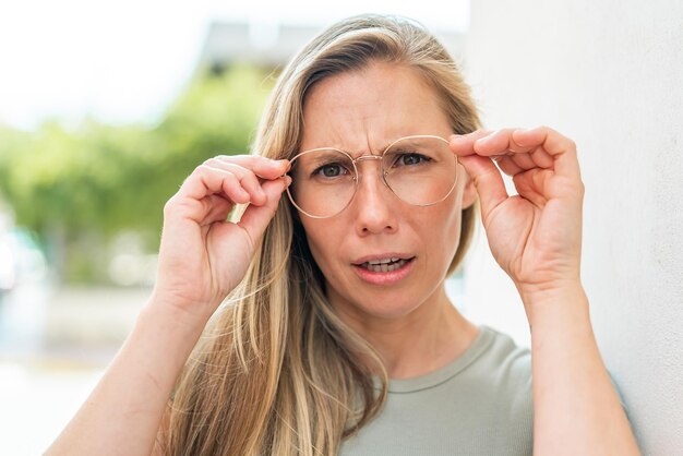 Junge blonde Frau im Freien mit Brille und frustriertem Gesichtsausdruck