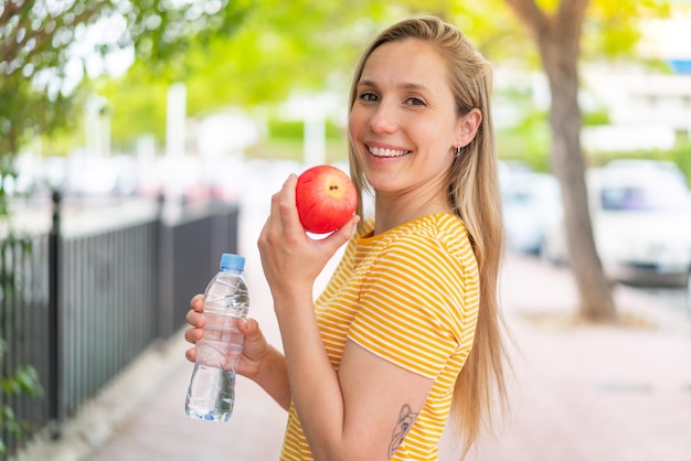 Junge blonde Frau im Freien mit einem Apfel und einer Flasche Wasser