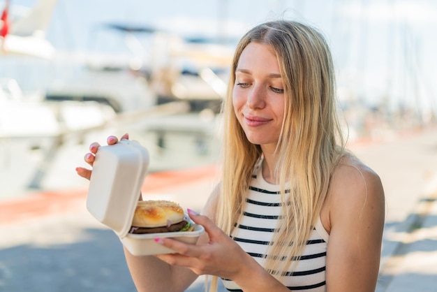 Junge blonde Frau im Freien mit einem Burger