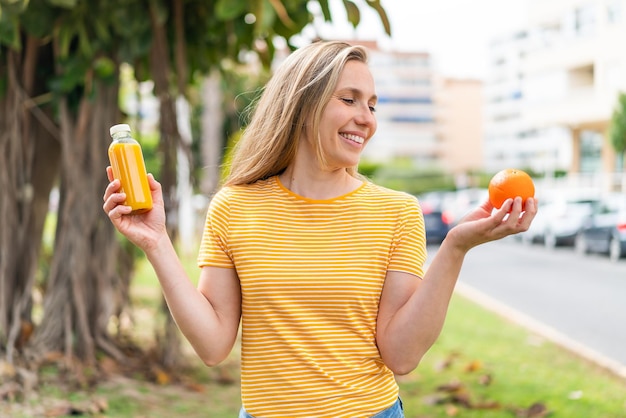 Junge blonde Frau im Freien mit einer Orange und einem Orangensaft