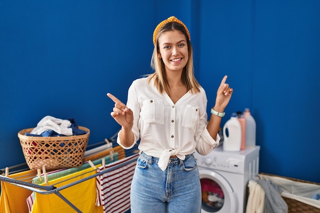 Junge blonde Frau in der Waschküche lächelt selbstbewusst und zeigt mit den Fingern in verschiedene Richtungen. Platz für Werbung kopieren