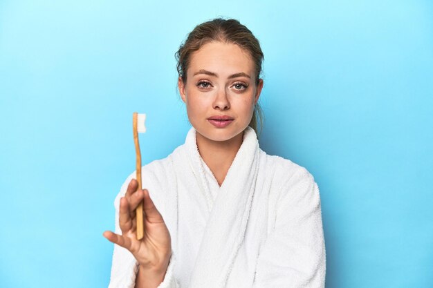 Junge blonde Frau in einem Gewand mit einer Zahnbürste in einem Studio