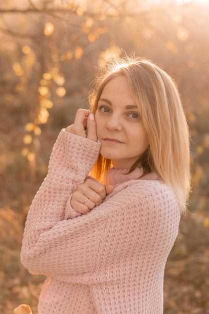 Junge blonde Frau in Jeans und einem warmen Pullover geht im Herbstwald romantischen Abend spazieren