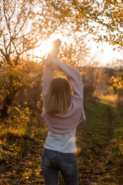 Junge blonde Frau in Jeans und einem warmen Pullover geht im Herbstwald romantischen Abend spazieren