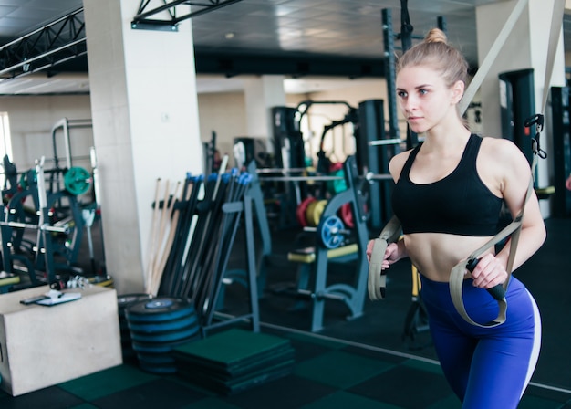 Junge blonde frau in sportbekleidung, die übung mit fitnessgurten in der turnhalle tut