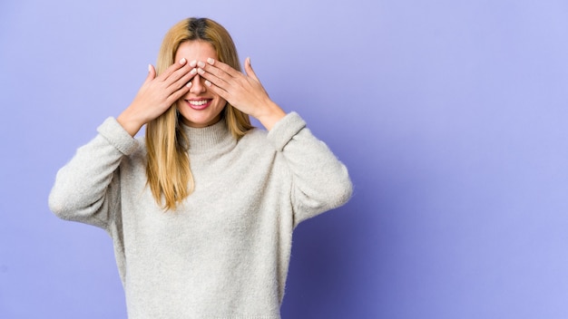 Junge blonde Frau isoliert auf lila Raum Angst, Augen mit Händen zu bedecken.