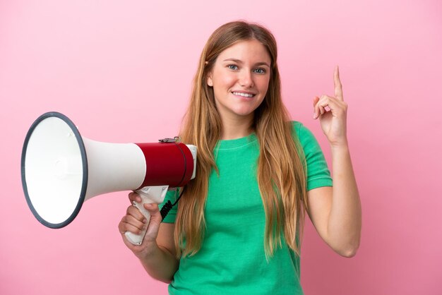 Junge blonde Frau isoliert auf rosa Hintergrund, die ein Megaphon hält und auf eine großartige Idee zeigt