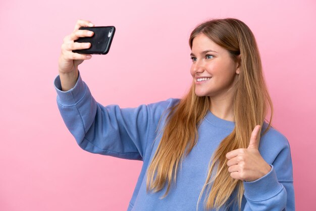 Junge blonde Frau isoliert auf rosa Hintergrund macht ein Selfie mit Handy